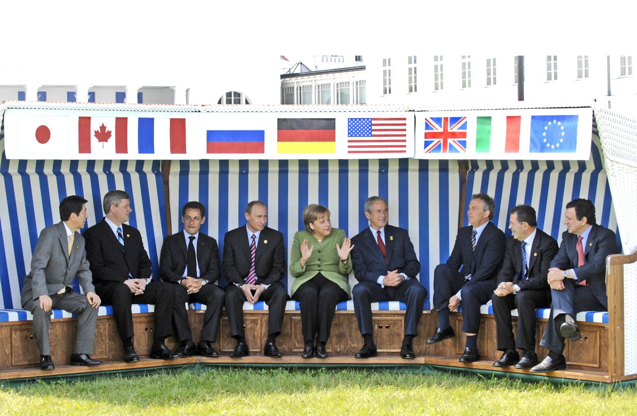 Farbfoto; Staats- und Regierungschefs des G8-Gipfels sitzen in drei aneinandergestellten Strandkörben ohne innere, seitliche Trennwände. Über ihnen auf weißem Stoffstreifen ist die jeweilige Landesflagge der darunter sitzenden Person abgebildet.