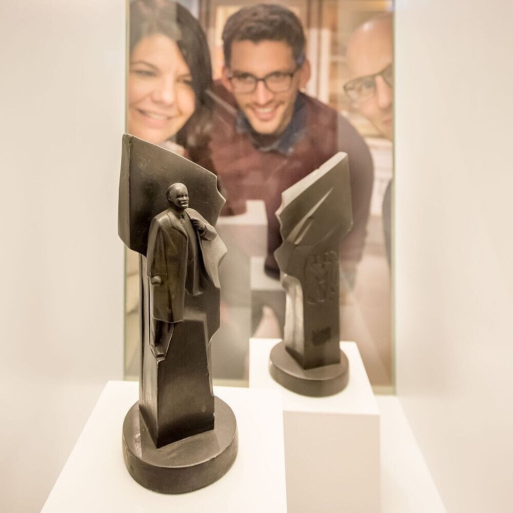 Two young men and a woman are looking at two small sculptures in a show case