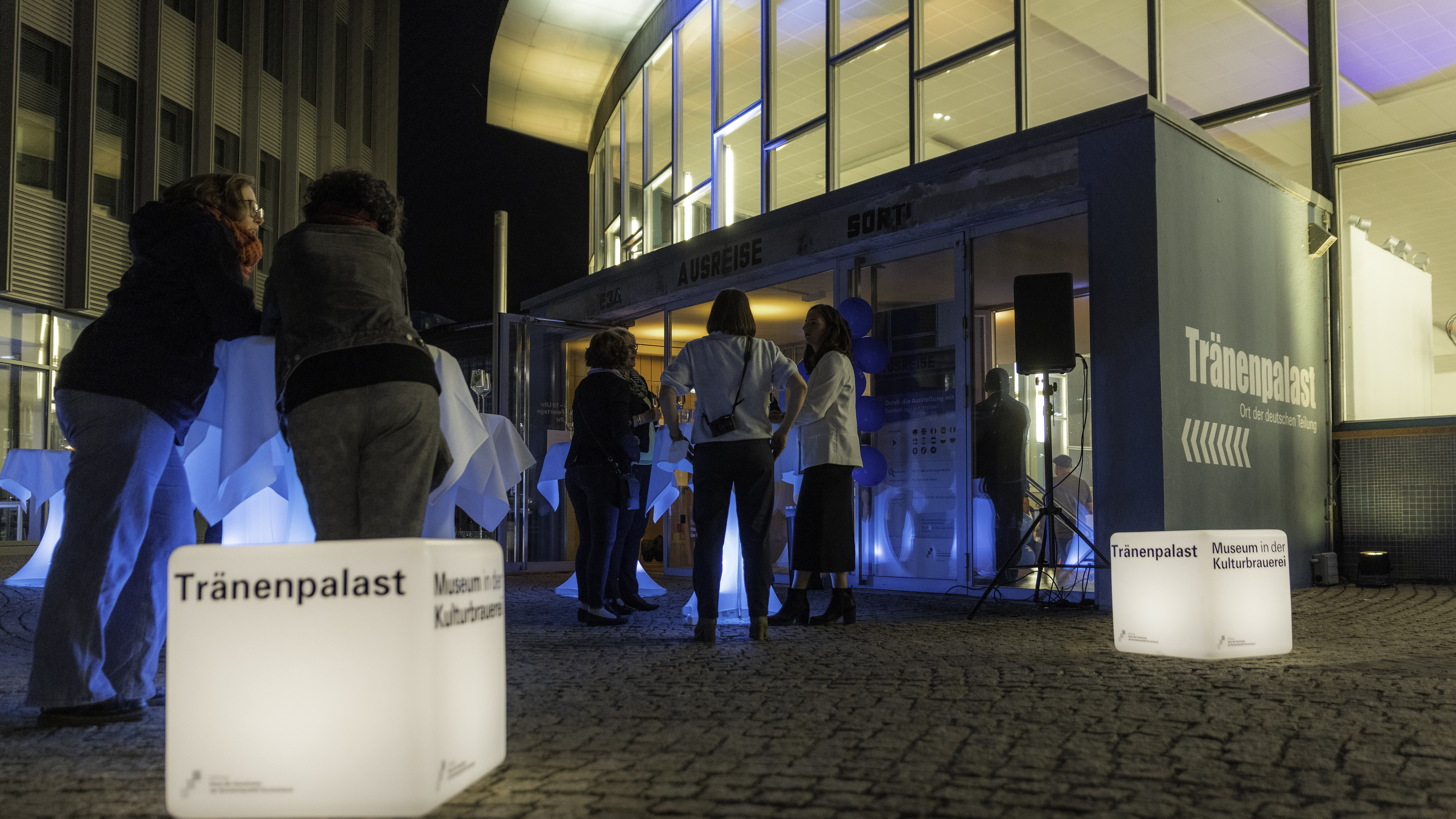 Leuchtende Würfel mit der Aufschrift "Tränenpalast" vor dem Eingang zum Tränenpalast. Dazu Menschen