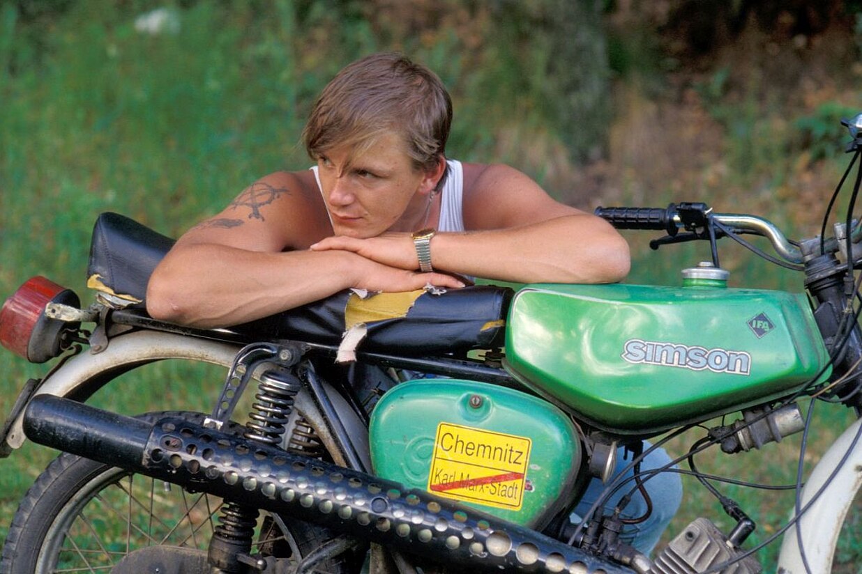 Ein junger Mann lehnt im Muskelshirt auf seinem Simson-Moped.