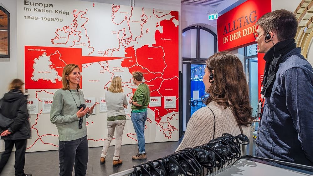 Besucherinnen und Besucher mit einem Guide in der Ausstellung. Im Hintergrund betrachten Besucherinnen und Besucher eine Karte zum Thema Europa im Kalten Krieg 1949-1989/90.