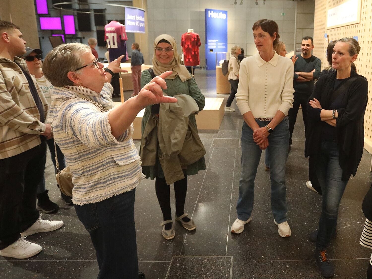 Vier Frauen stehen im Halbkreis eine fünfte Frau herum, die zu ihnen spricht und mit erhobenen Armen gestikuliert. 