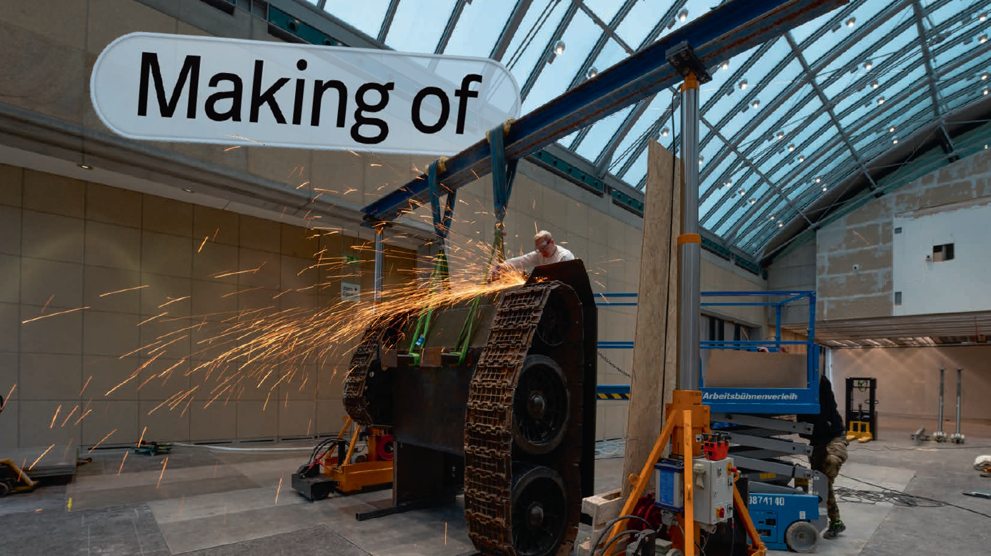 In der Ausstellungshalle arbeitet ein Mann an einem Ausstellungsstück mit Panzerketten, wobei Funken sprühen