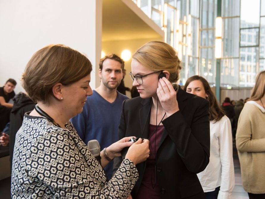 Eine junge Frau befestigt den Ohrstecker den Audio-Gruppenführungssystems, eine andere Frau hilft ihr dabei
