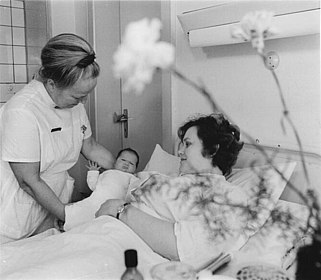 Kinderkrankenschwester und Mutter mit Neugeborenem im Krankenhausbett in schwarz/weiß
