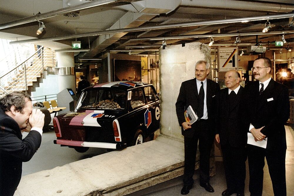 Blick in die Ausstellung mit Fotograf, Mauerteilen, einem Trabi sowie Stiftungspräsident Hermann Schäfer, Beiratsvorsitzendem Lothar Gall und dem Direktor des ZFL, Rainer Eckert