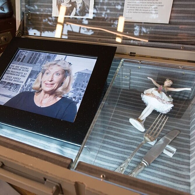 An open suitcase, the tablet on the left is showing a video of the contemporary witness Sigline, on the right a small porcelain figure.