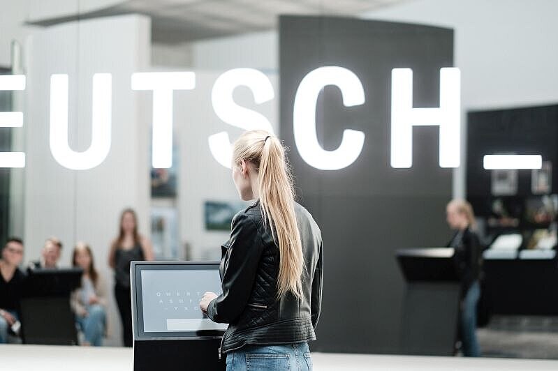 Eine junge Frau steht an einem Bedienungsterminal vor einer glänzenden LED-Wand