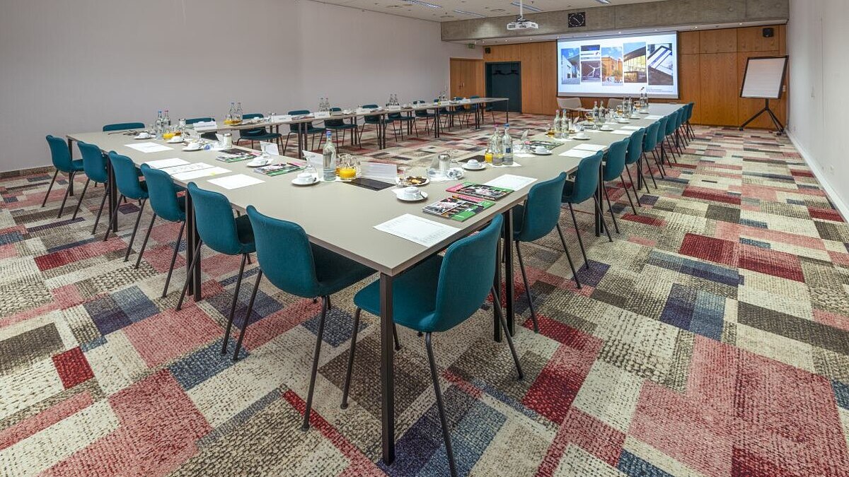 Ein Konferenzraum mit Tischen in U-Form und Stühlen ausgerichtet auf eine Leinwand
