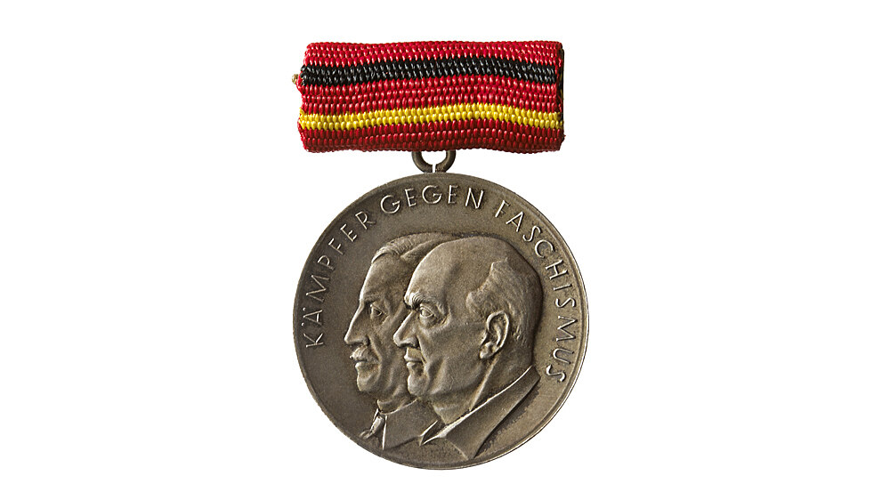 Silberfarbener Medaille. Auf der Vorderseite sind Kopfbilder von Ernst Thälmann und Rudolf Breitschei im Profil abgebildet mit der Umschrift: 'Kämpfer gegen Faschismus'. Auf der Rückseite die Abbildung des Staatssymbols der DDR (Hammer und Zirkel), Umschrift: 'Vorwärts und nicht vergessen 1933-1945'. 