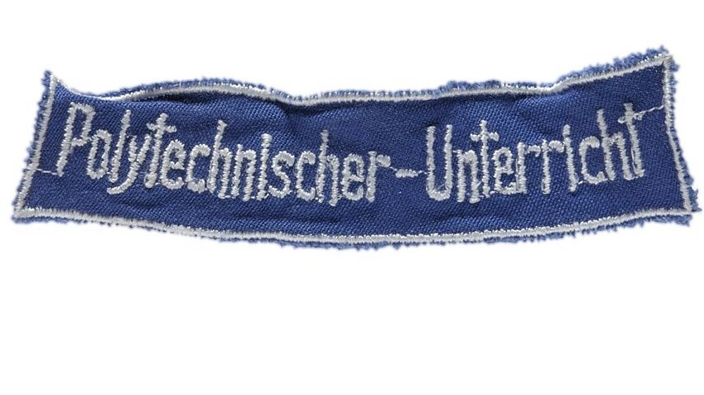 Blauer Aufnäher mit weißem Rand und weißer, gestickter Schrift: 'Polytechnischer-Unterricht'.