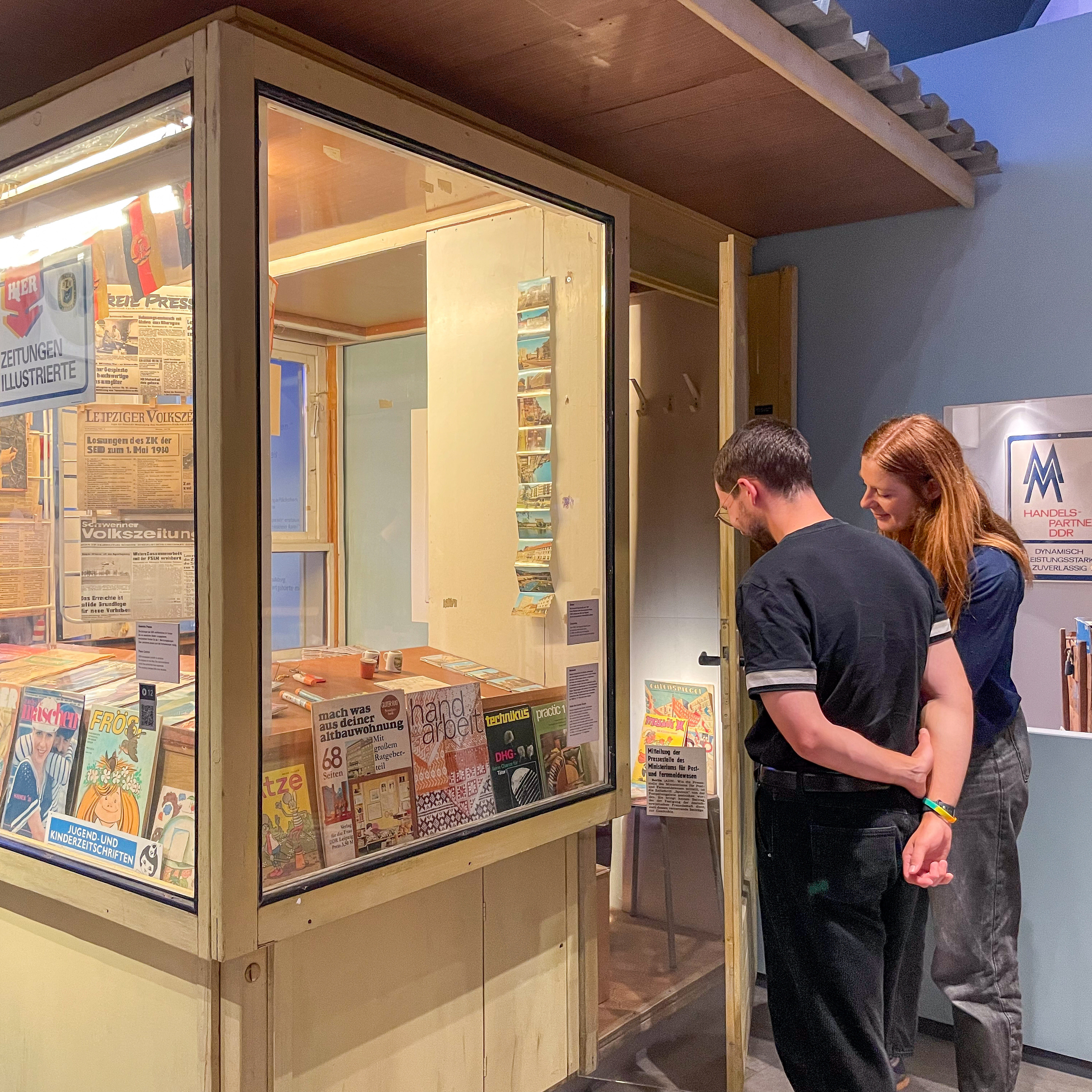 Ein Besucher und eine Besucherin einer Gruppe betrachten Zeitschriften in einem Kiosk in der Ausstellung.