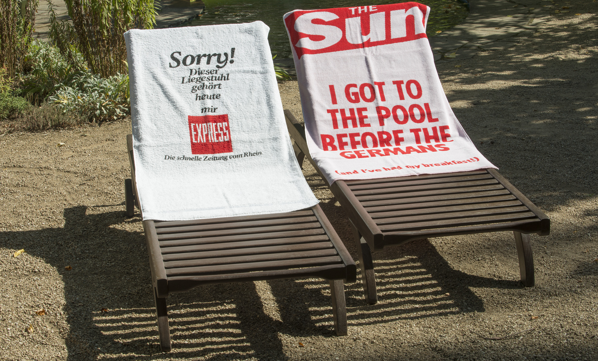  Two deck chairs with towels, one by the German newspaper Express, "Sorry, dieser Liegestuhl gehört heute mir!" and one by the british newspaper "The Sun", "I got to the pool before the Germans".
