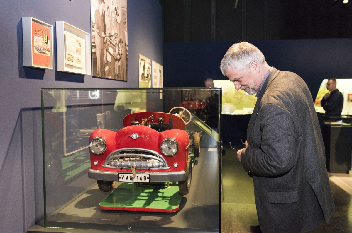 Ein Mann blickt in eine Vitrine, in der ein Auto-Modell aus Metall steht, etwa in der Größe eines Bobby Cars