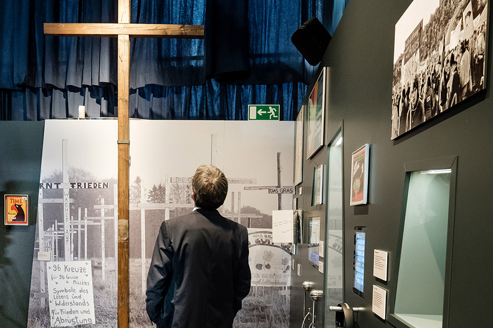 Ein Besucher betrachtet in der Ausstellung ein großes Holzkreuz der Friedensbewegung.