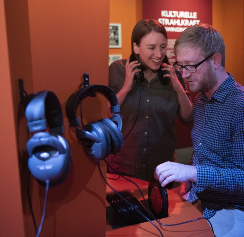 Two visitors are sitting at the sound bar and look through the records.