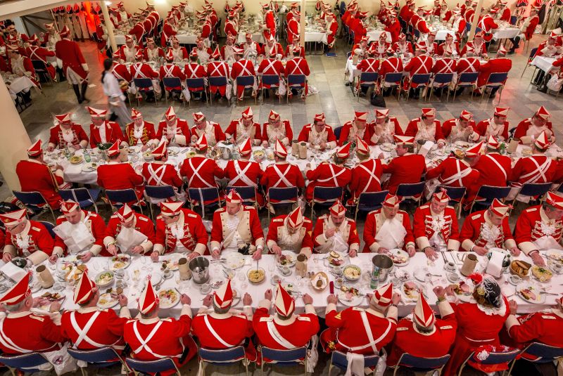 Men in red and white carnival uniforms sit at long tables and eat.