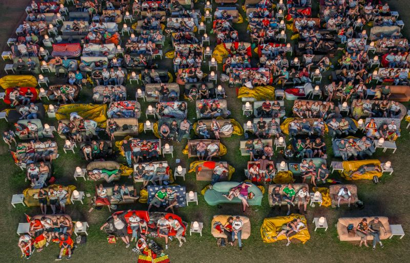 "Rudelgucken" zur Fußballweltmeisterschaft 2014 in Berlin Menschen sitzen auf in Reihen angeordneten Sofas auf einem Rasen, teilweise mit Deutschlandfahnen.