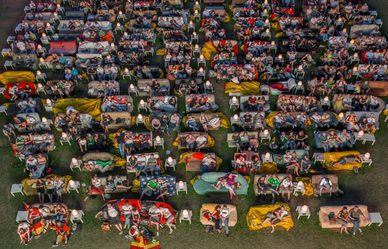 People sit on sofas arranged in rows on a lawn, partly with German flags.