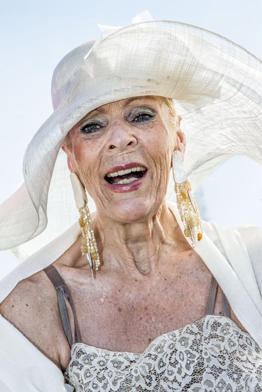 An elderly lady with a large white hat and eye-catching golden earrings.