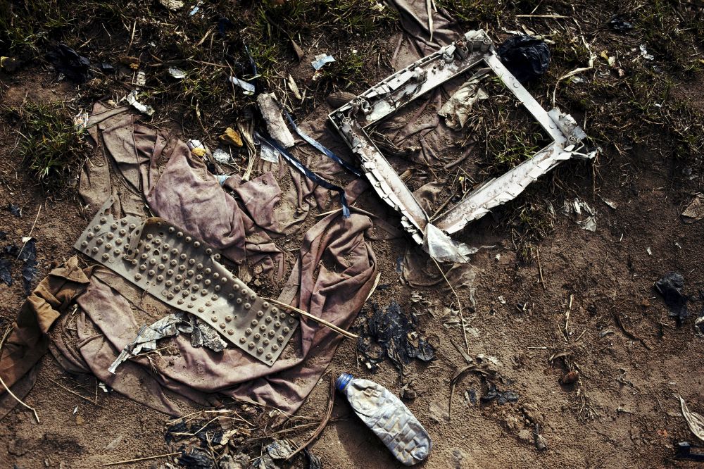 Rubbish, including what appears to be the remains of a monitor, lies on a floor of earth and grass.