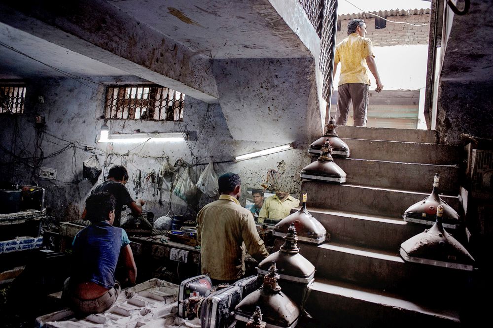 In a cellar room there are numerous dismantled screen tubes, two men seem to be working on them.