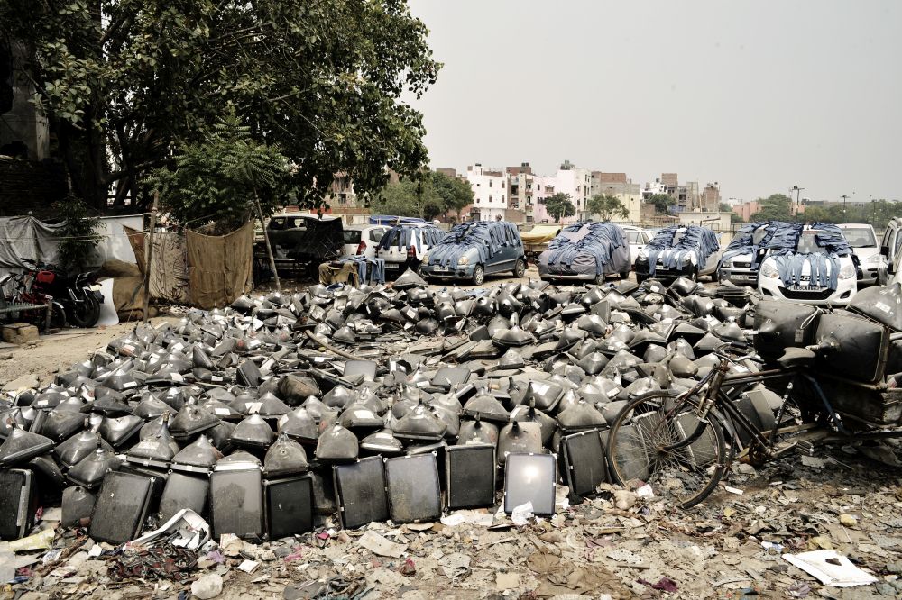 In front of parked cars is a large pile of screen tubes, in the background are houses.