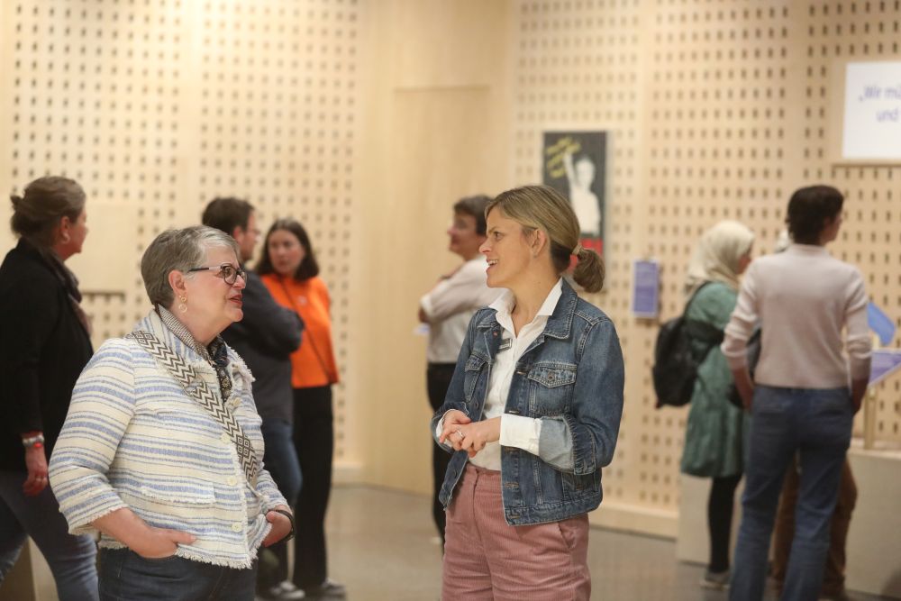 Im Vordergrund zwei Frauen, die sich unterhalten, im Hintergrund weitere Menschen