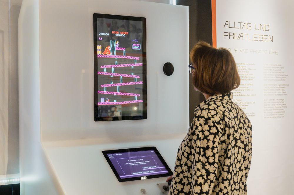 A visitor stands in front of a wall screen on which a Donkey-Kong-Video-game is running.