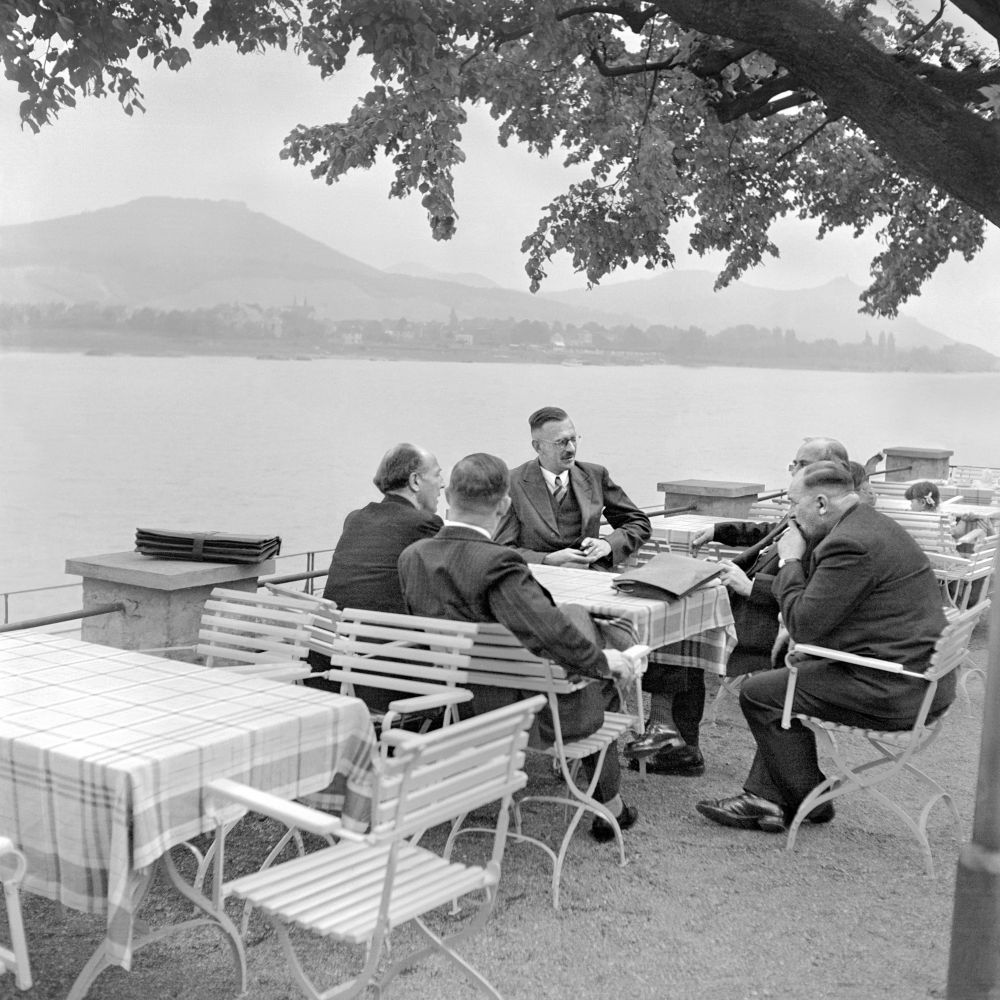 Fünf Männer mittelren Alters sitzen an einem Tisch in einem Biergarten am Bonner Rheinufer.