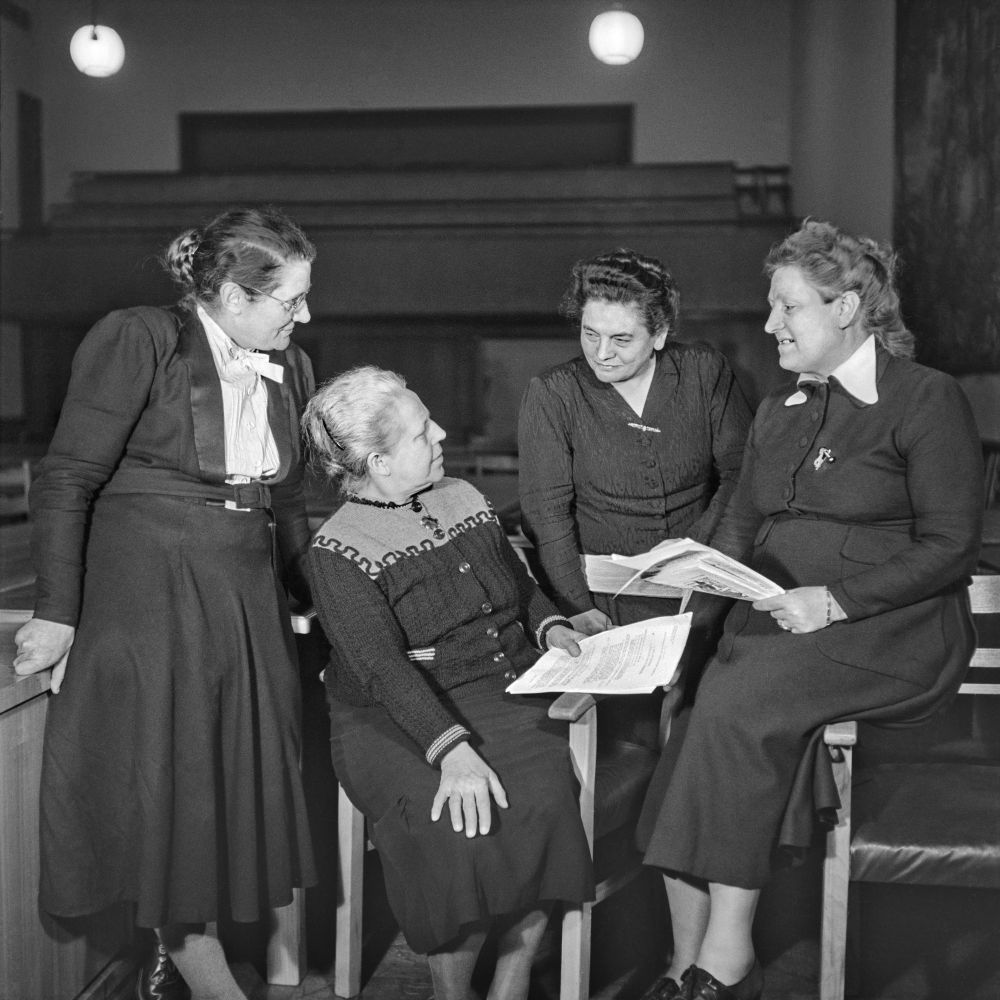 Helene Wessel, Helene Weber, Friederike Nadig und Elisabeth Selbert sitzen und stehen zusammen und sehen sich an.