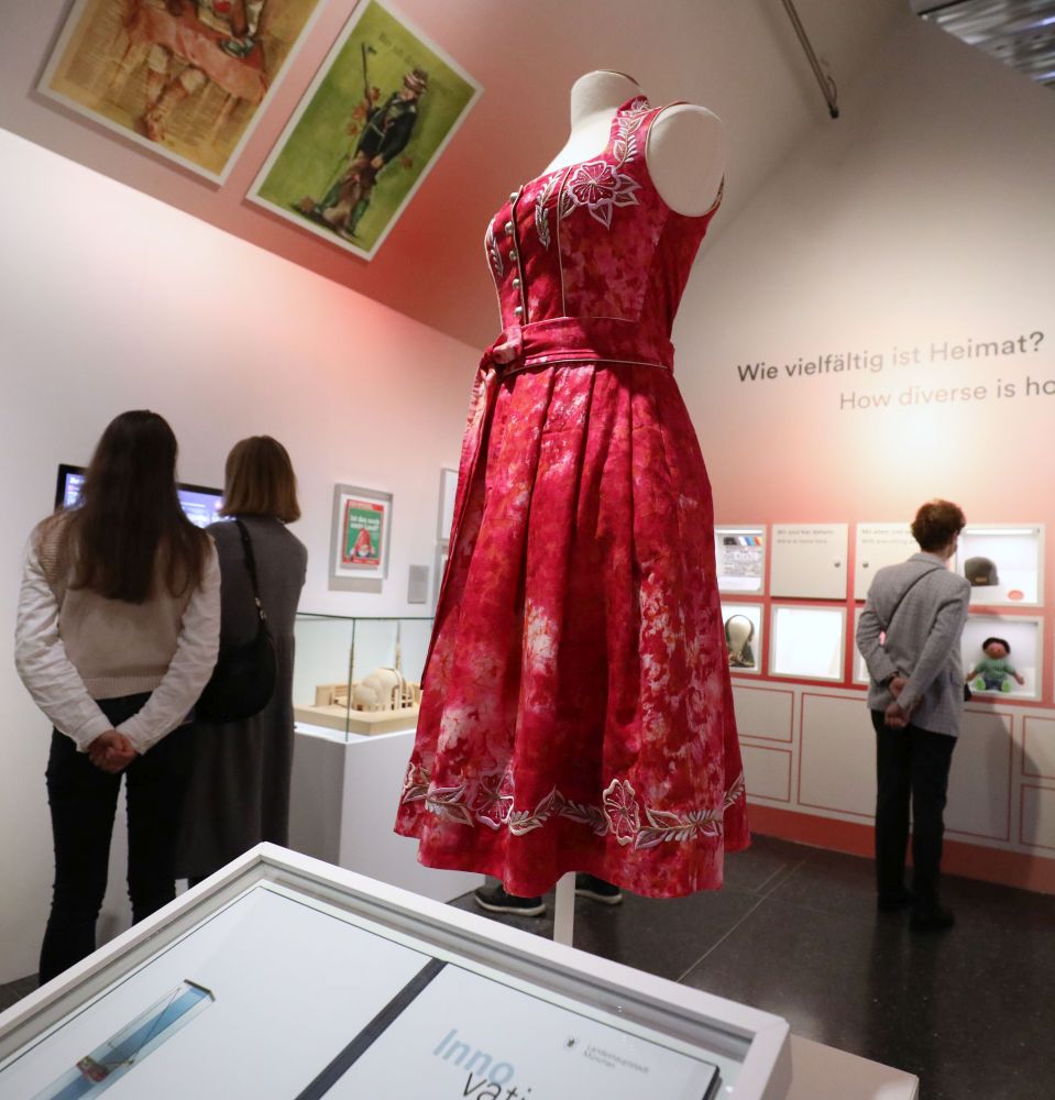 Ein Dirndl, das aus einem roten Batik-Stoff geschneidert ist, steht auf einer Schneiderpuppe in der Mitte des Ausstellungsraumes.