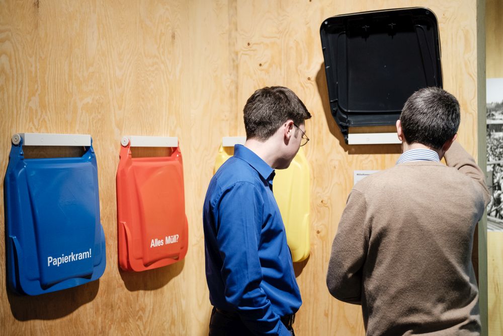 Besucher schauen sich Mülltonnendeckel mit Informationen zur Mülltrennung an