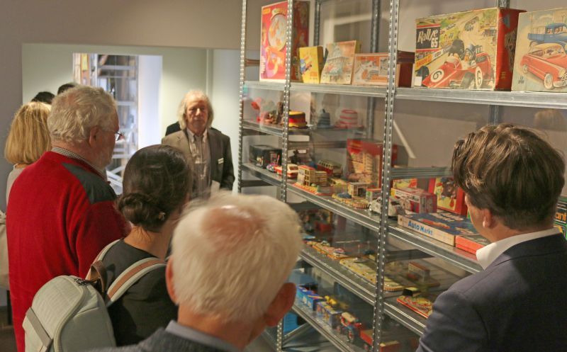 People stand in front of a metal shelf full of model cars, model multi-storey car parks and colorful play boxes.