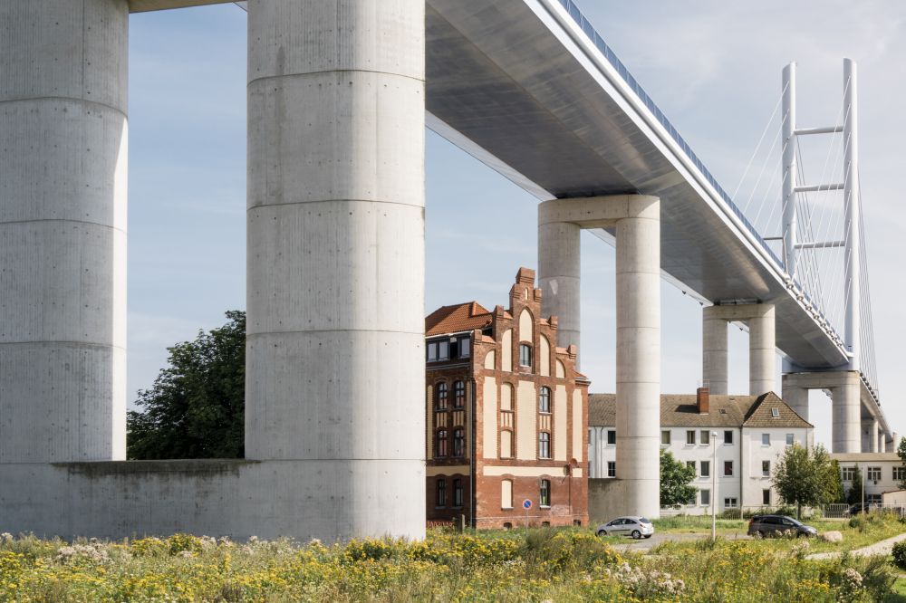 Unter einer hohen, modernen Betonbrücke stehen mehrere Häuser.