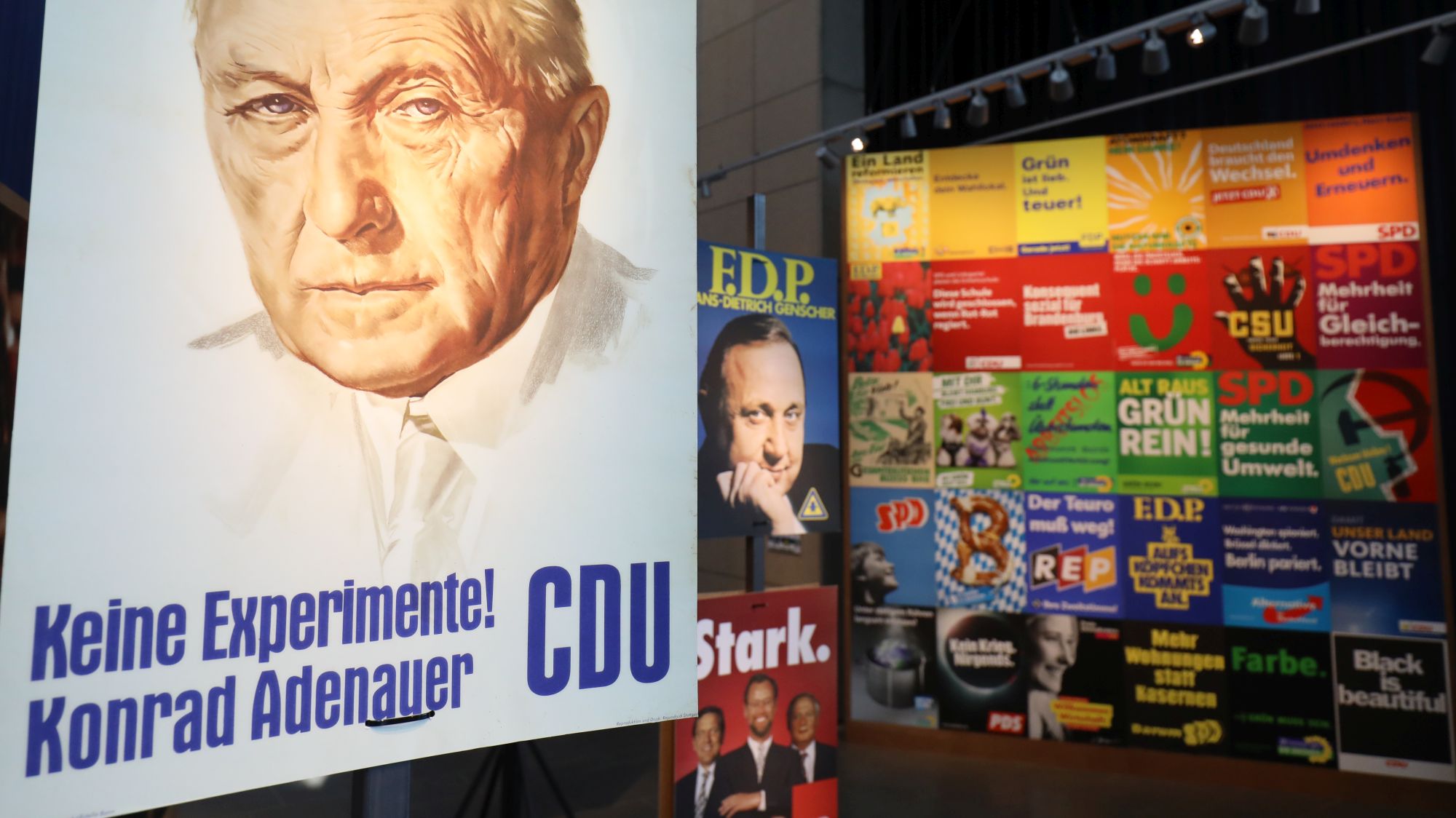 Das berühmte CDU-Plakat mit Konrad Adenauer und dem Slogan Keine Experimente und eine große Wand mit vielen weiteren Plakaten im Hintergrund.
