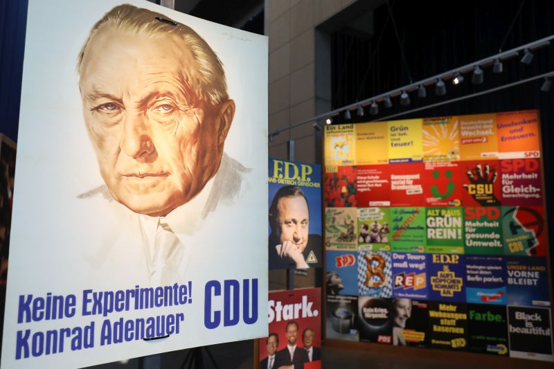 Das berühmte CDU-Plakat mit Konrad Adenauer und dem Slogan Keine Experimente und eine große Wand mit vielen weiteren Plakaten im Hintergrund.