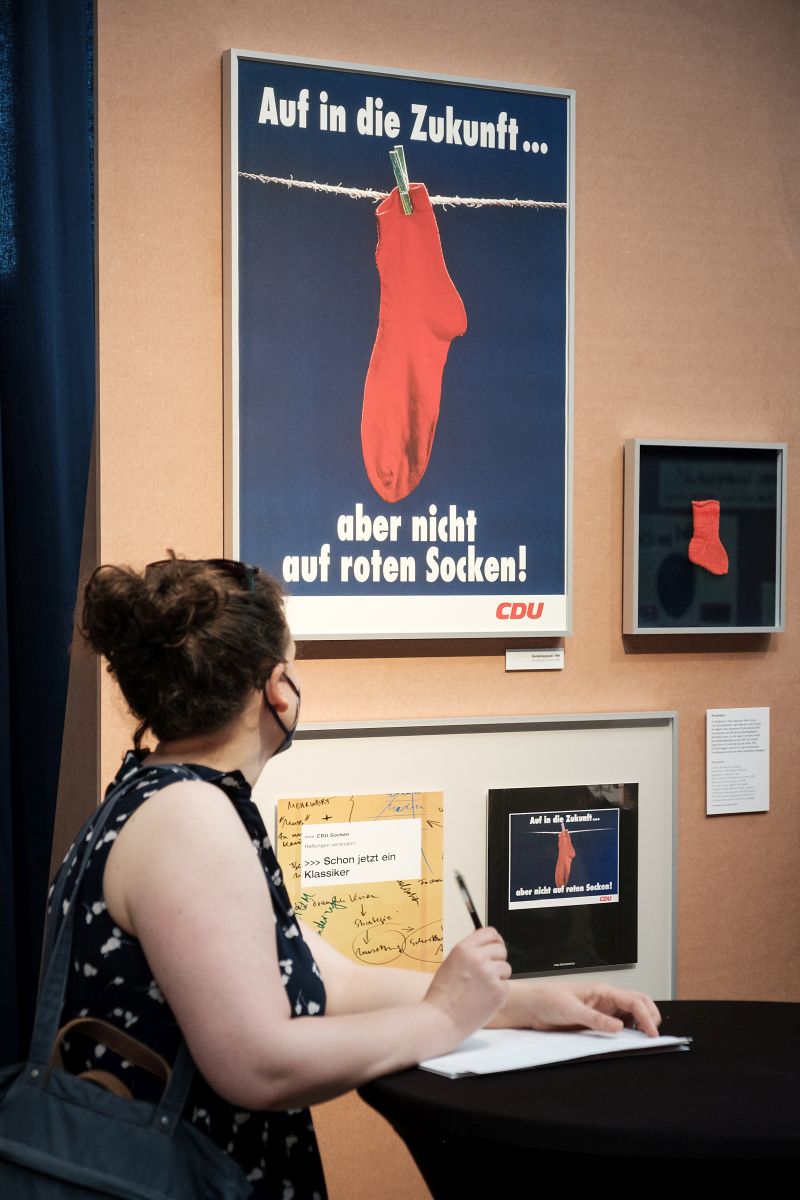 Eine Frau blickt auf ein CDU-Wahlplakat mit einem roten Socken an einer Wäscheleine. 