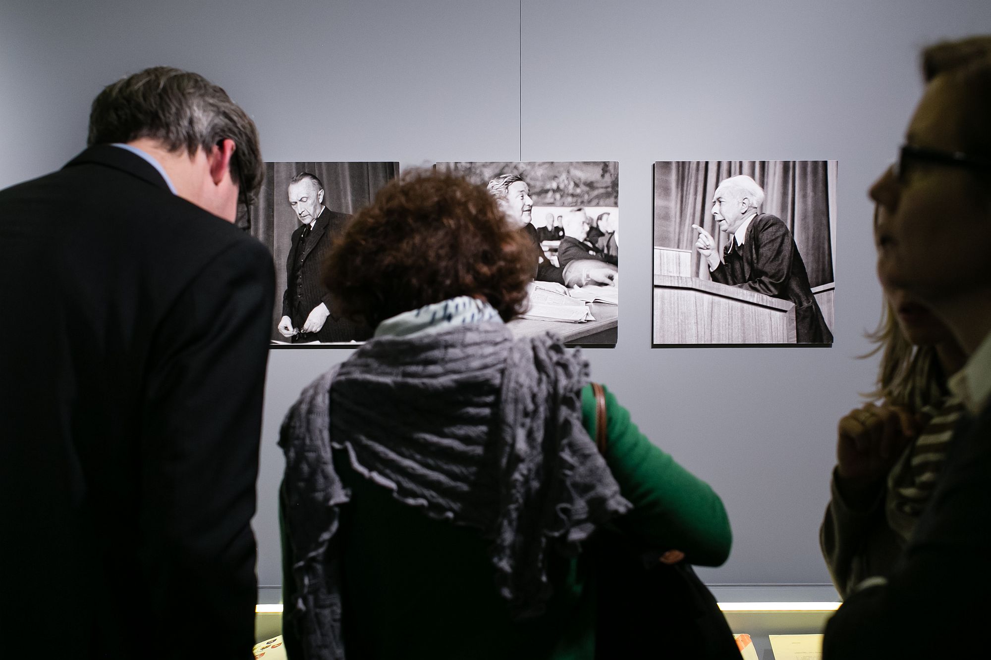 Ein Mann und zwei Frauen stehen vor einer Wand mit Fotografien von Konrad Adenauer, Carlo Schmid und Theodor Heuss.
