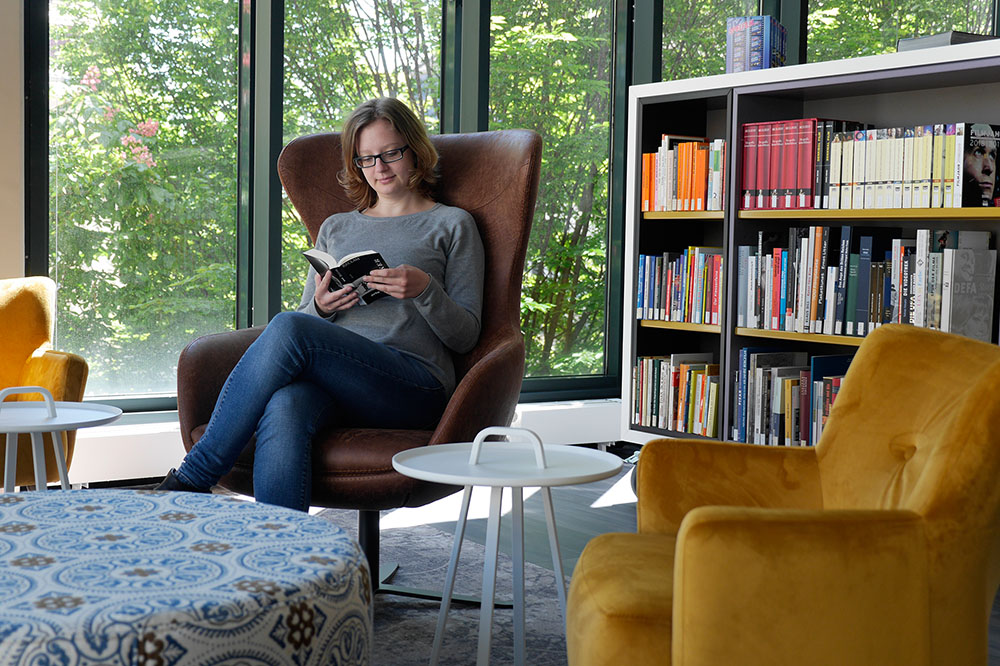 Eine Besucherin sitzt im Sessel mit einem Buch in der Lounge