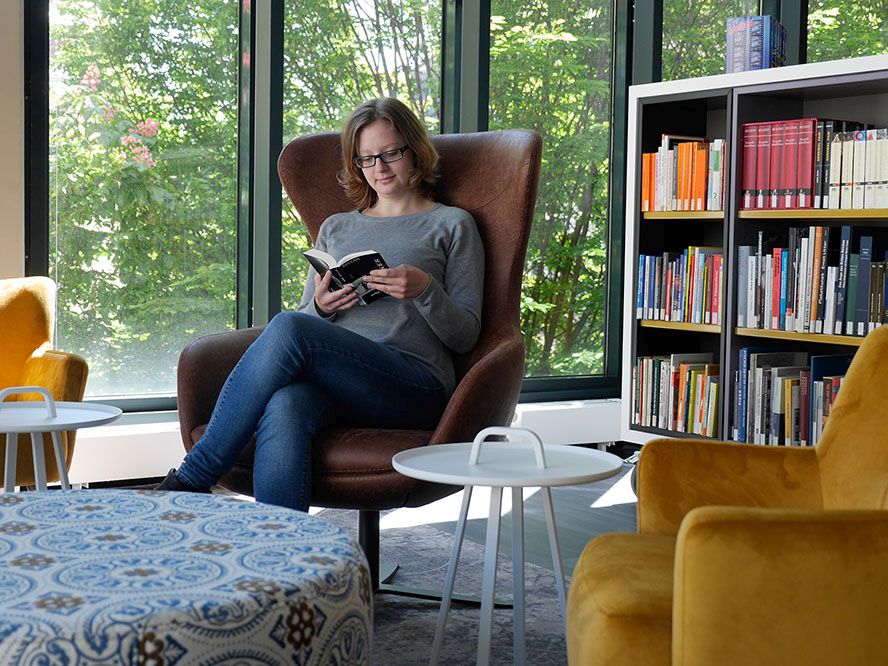 Eine Besucherin sitzt in einem gemütlichen Sessel mit einem Buch in der Lounge