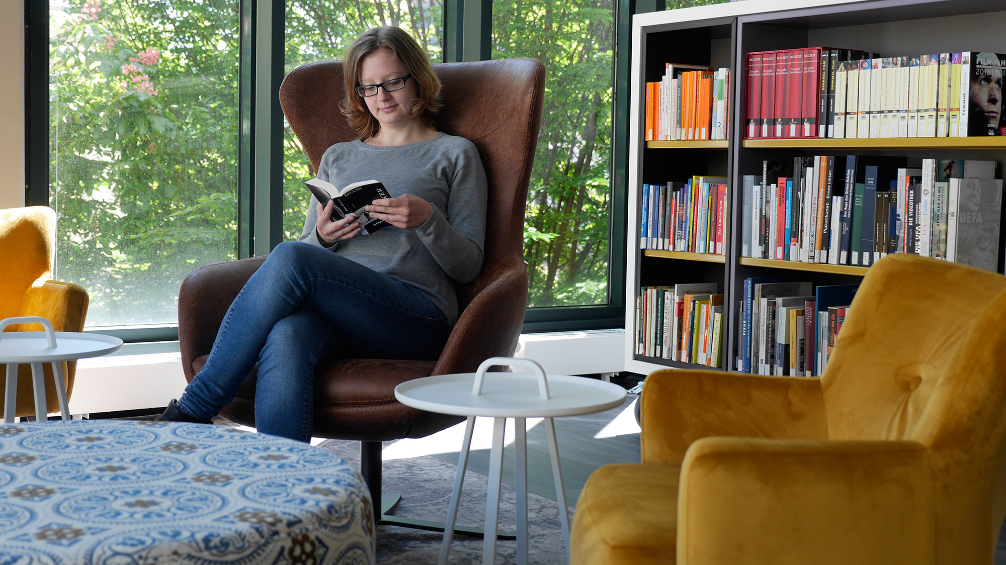 Eine Besucherin sitzt im Sessel mit einem Buch in der Lounge