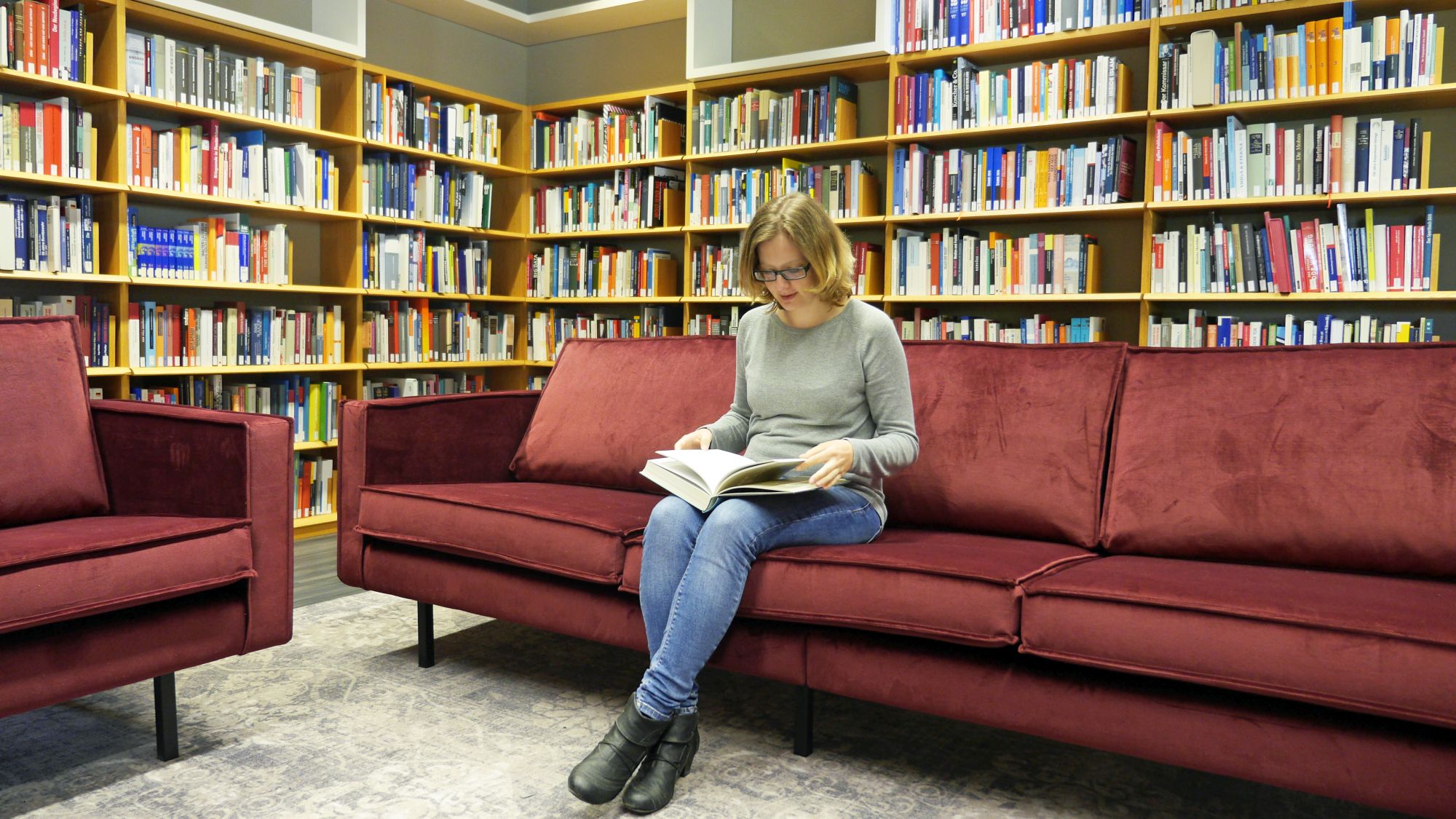 Eine Besucherin sitzt auf einem gemütlichen Sofa und liest