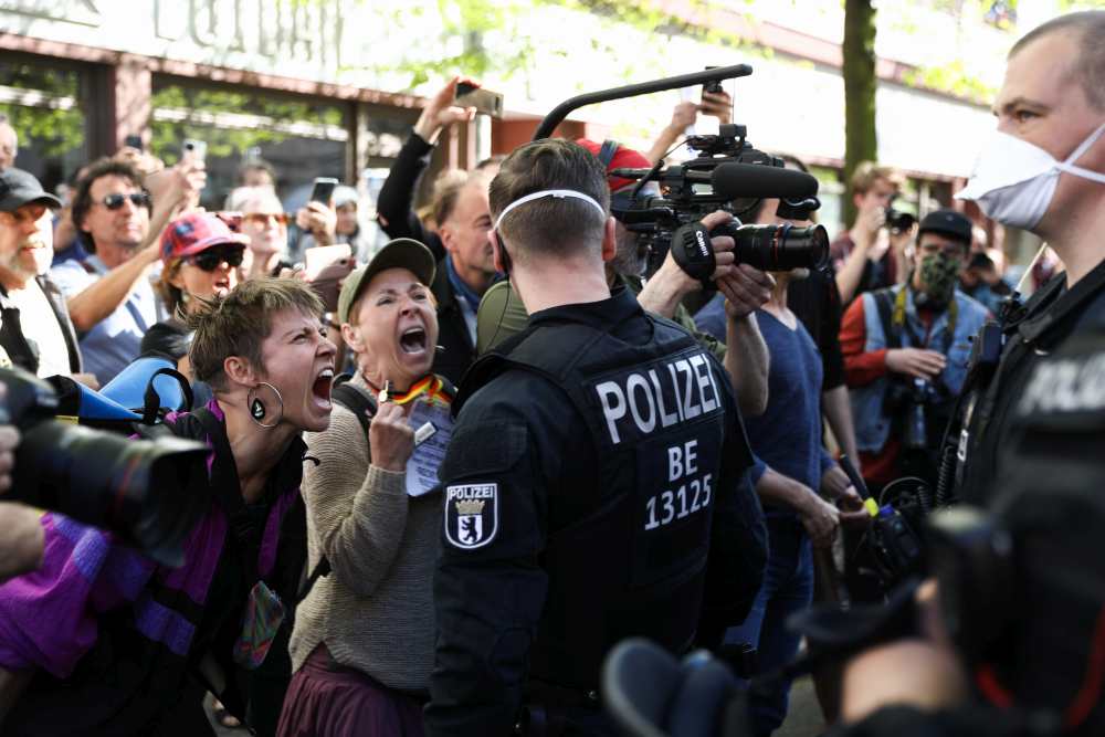 Demonstrantinnen ohne Mund-Nasen-Schutz schreien bei einer Demo gegen die Corona-Maßnahmen in Berlin einen Polizisten an.