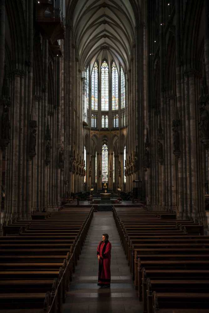 Ein Domschweizer steht im leeren Kölner Dom und blickt in Richtung Tür.