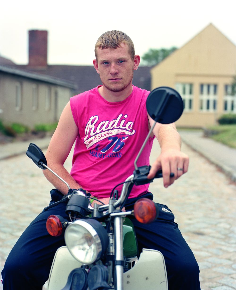 Junger Mann in pinkfarbenen ärmellosem Top sitzt auf Motorroller. und schaut in die Kamera.