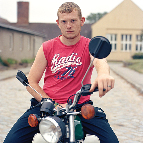 Junger Mann in pinkfarbenen ärmellosem Top sitzt auf Motorroller. und schaut in die Kamera.