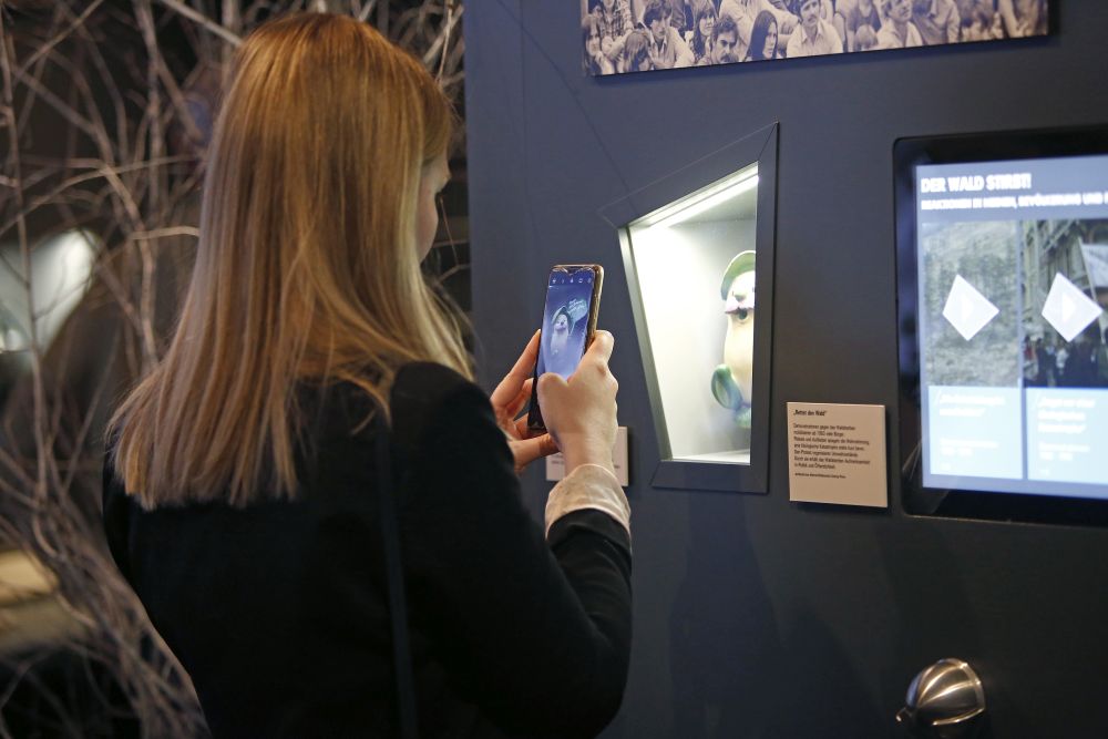 Besucherin fotografiert ein Objekt zum Thema Waldsterben in der Ausstellung