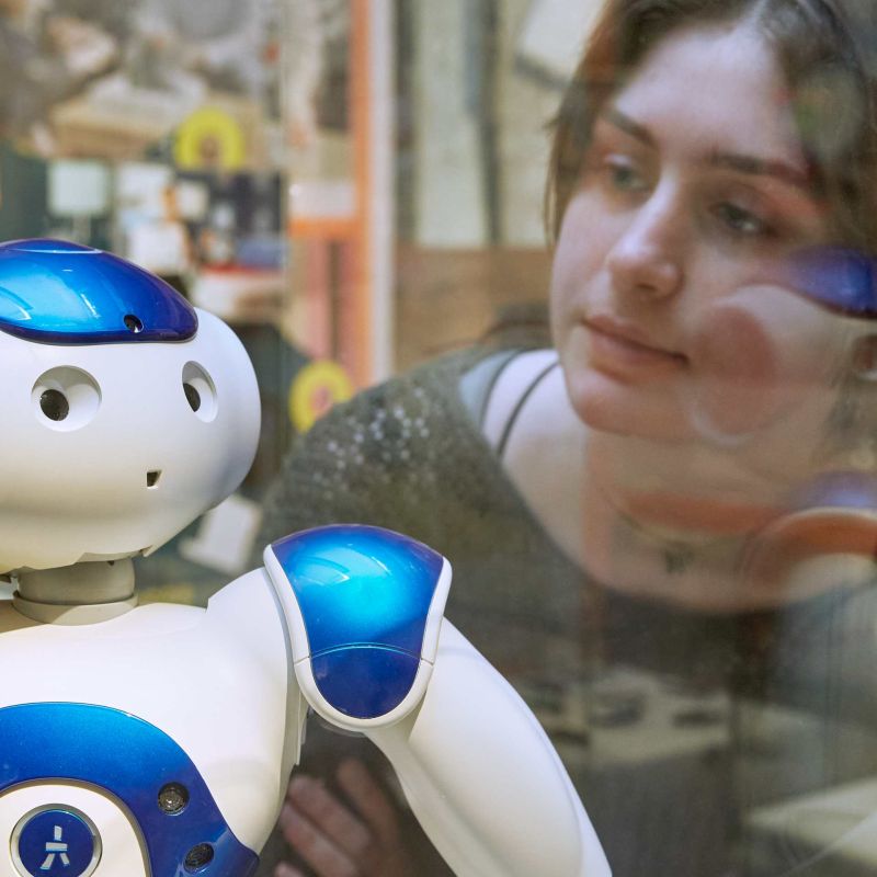 Junge Frau in der Ausstellung vor Vitrine mit Roboter