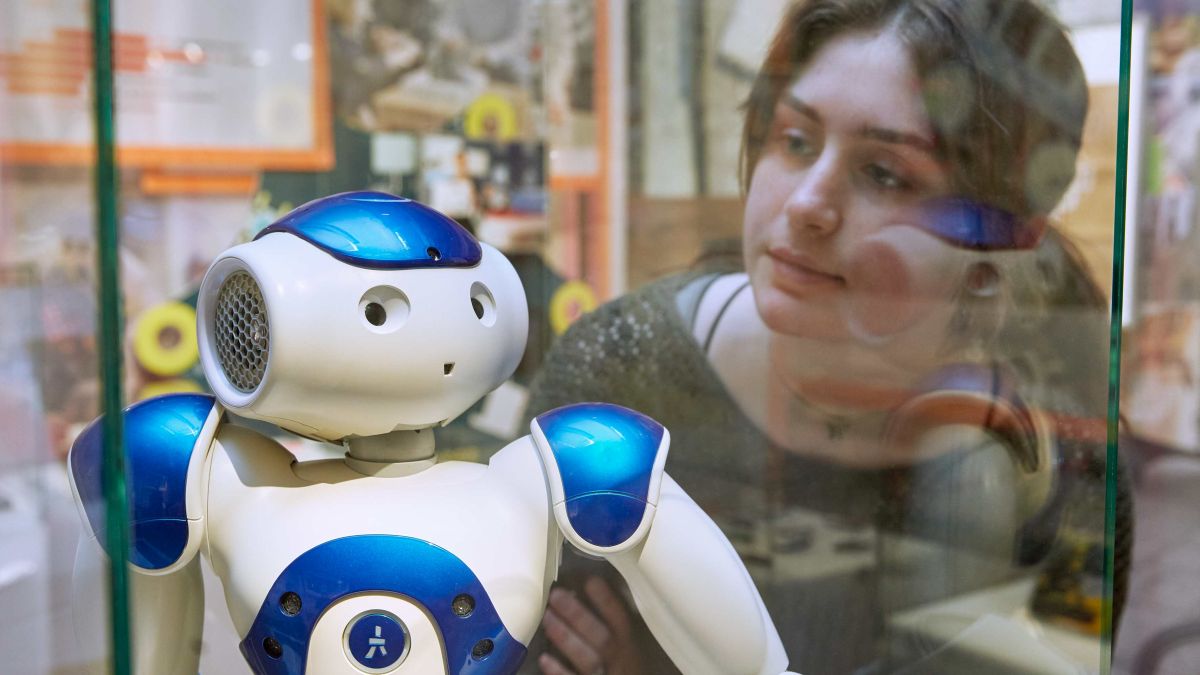 Junge Frau in der Ausstellung vor Vitrine mit Roboter